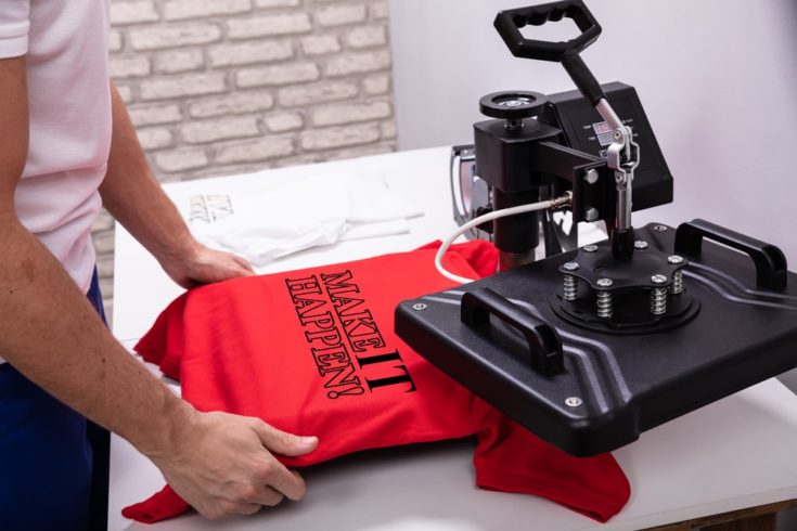 Man printing on a red t shirt in workshop using heat press machine