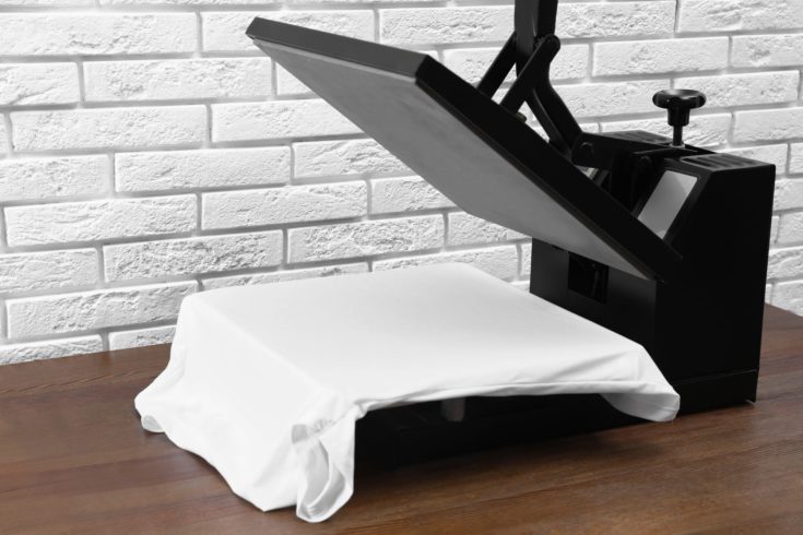 Heat press machine with t-shirt on wooden table near white brick wall