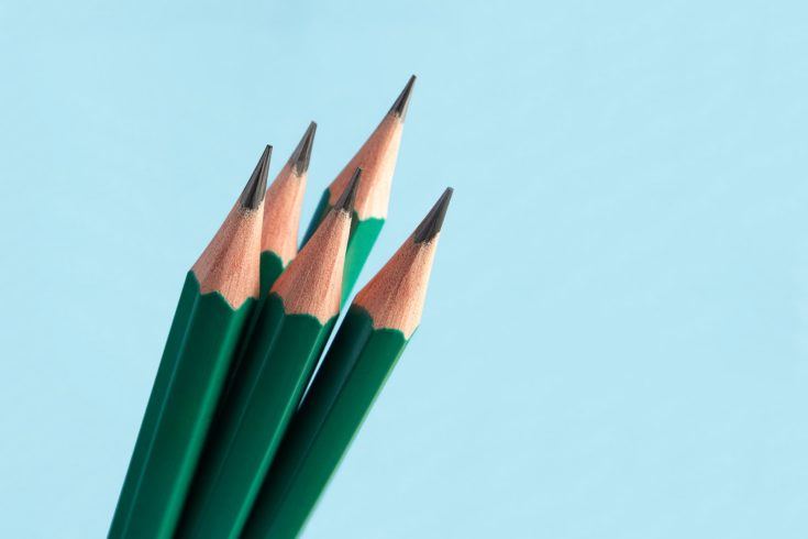 Few of classic graphite sharply sharpened pencils, in green wooden shell, on blue background.